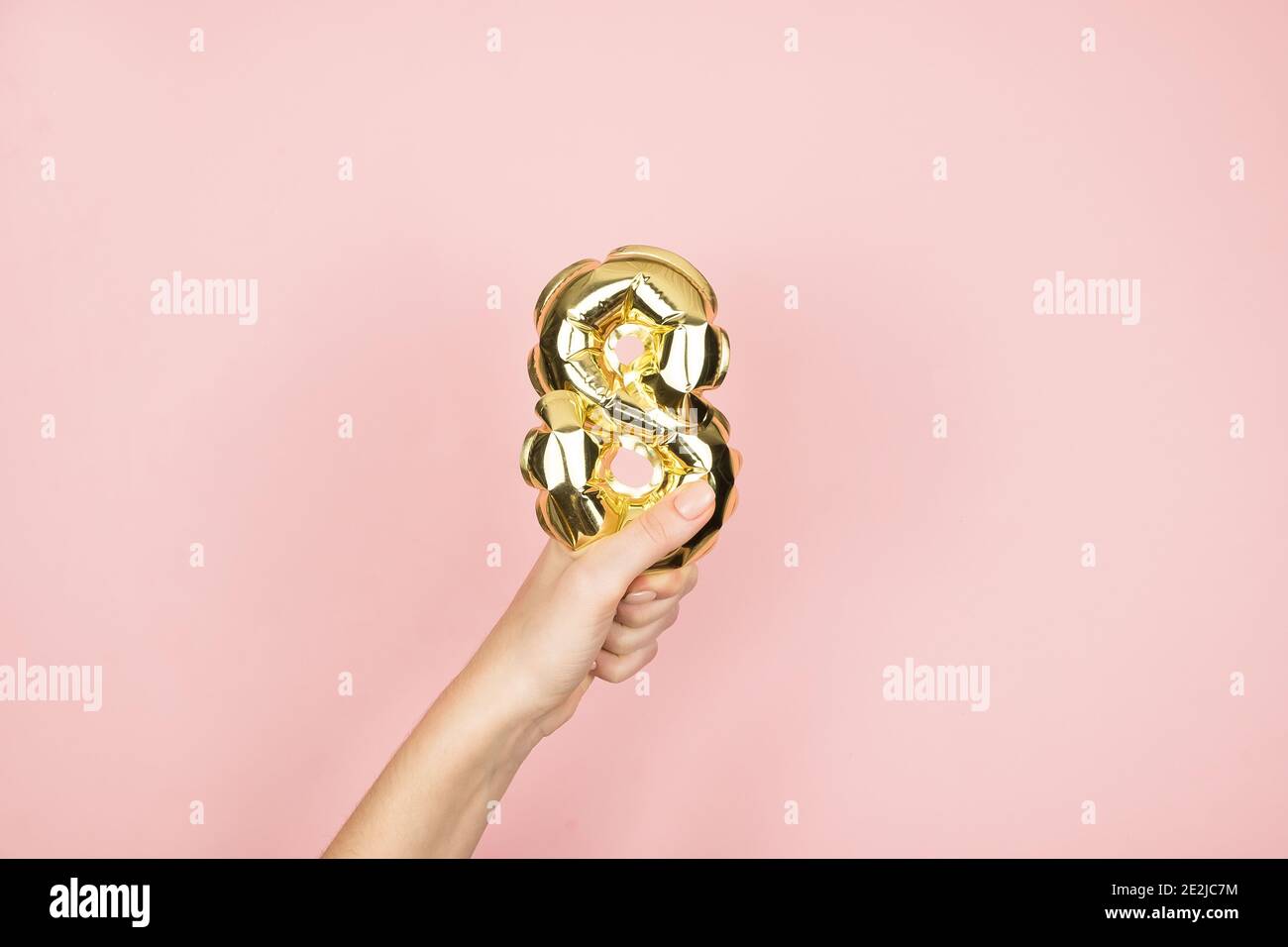 Palloncini in lamina d'oro numero 8 in mano femina su sfondo rosa. Buon giorno delle donne Foto Stock