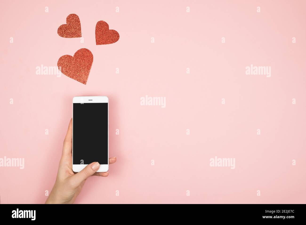 San Valentino concetto giorno, cellulare in mano schermo con cuori rossi su sfondo rosa. Amore nei social media Foto Stock