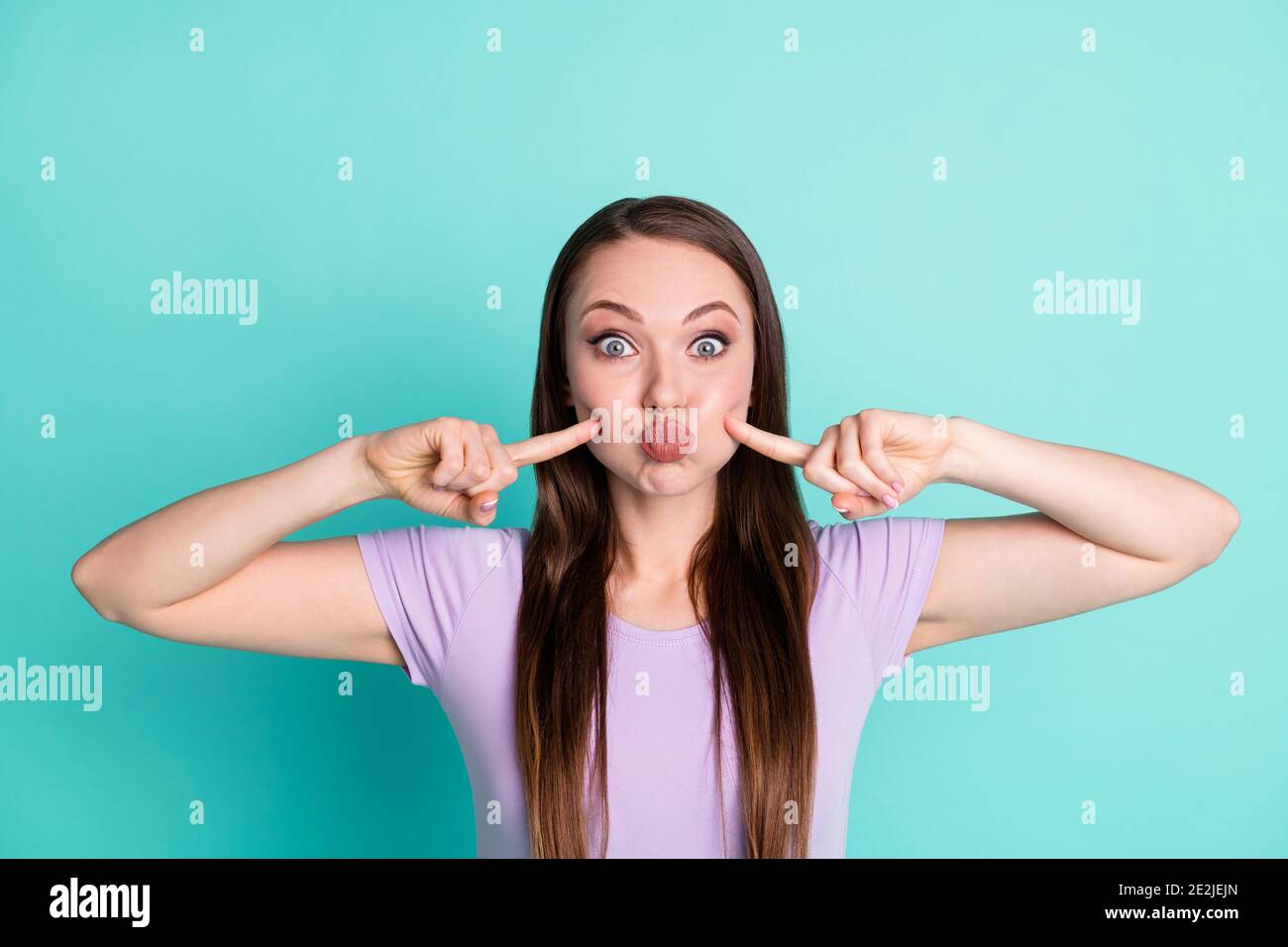 Ritratto fotografico di ragazza divertente che tiene le guance d'aria che le toccano con le dita isolate su un vivace sfondo di colore teal Foto Stock