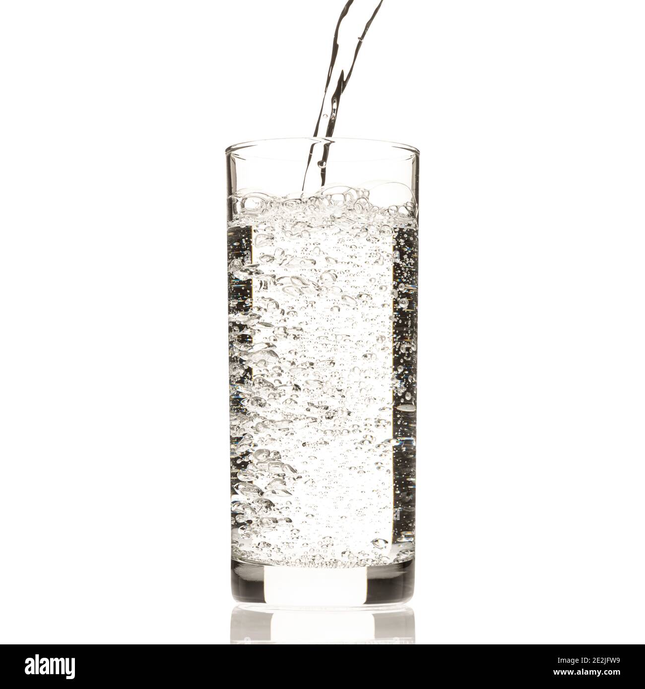 L'acqua viene versata in un bicchiere alto, creando bolle, appoggiate su uno sfondo bianco. Foto Stock
