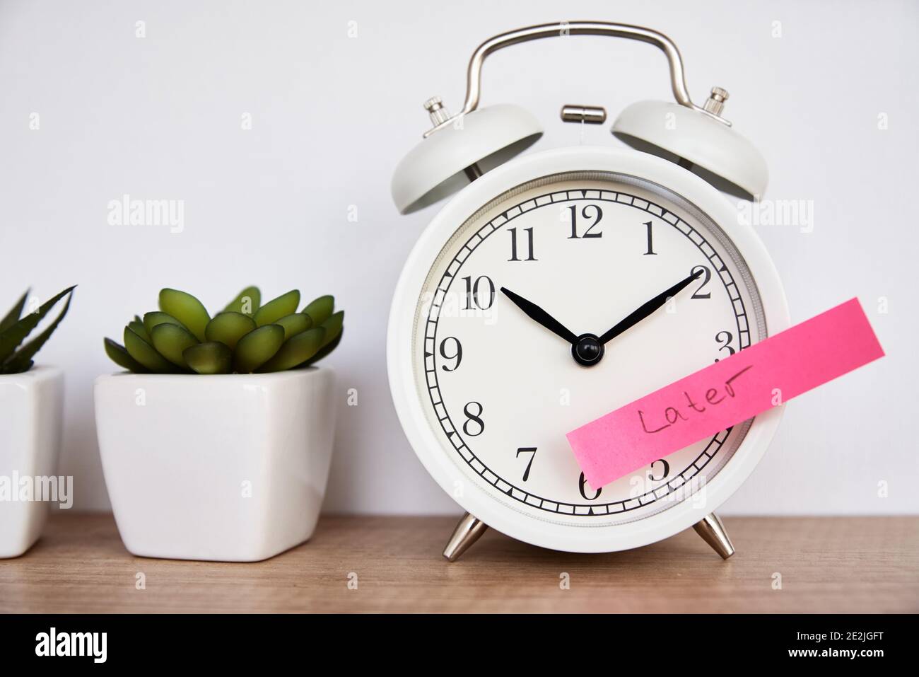 Concetto di procrastinazione e ritardo. Nota appiccicosa con parola più tardi sulla sveglia bianca. Tempo di urgenza Foto Stock