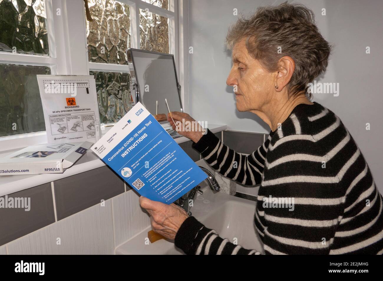 Inghilterra, Regno Unito. 2021. Donna in bagno che studia le istruzioni di un Coronavirus, Covid-19 Home Test kit Foto Stock