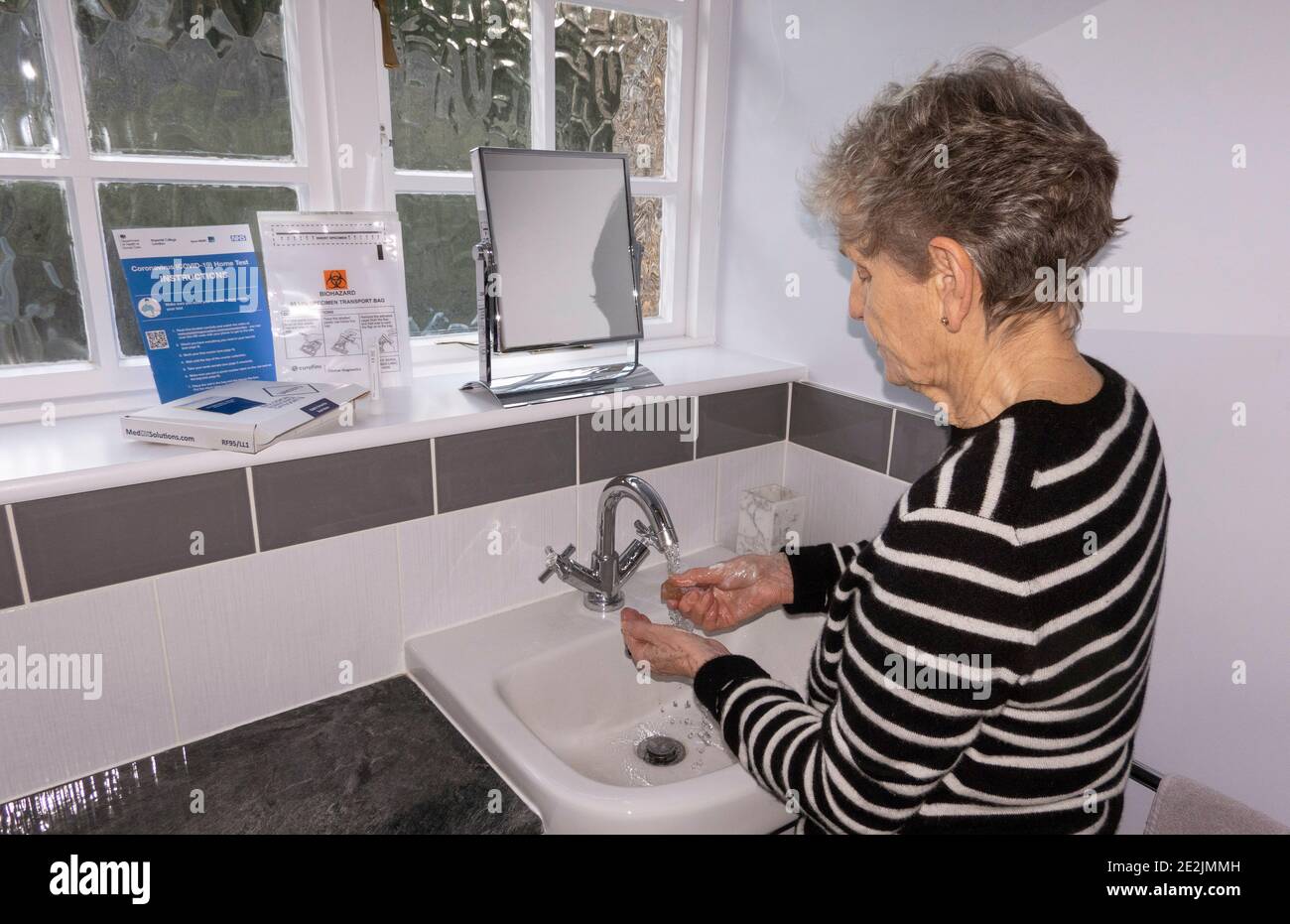 Inghilterra, Regno Unito. 2021. Una donna anziana che si lava le mani prima di fare un test di coronavirus domestico da oggetti sul davanzale. Foto Stock