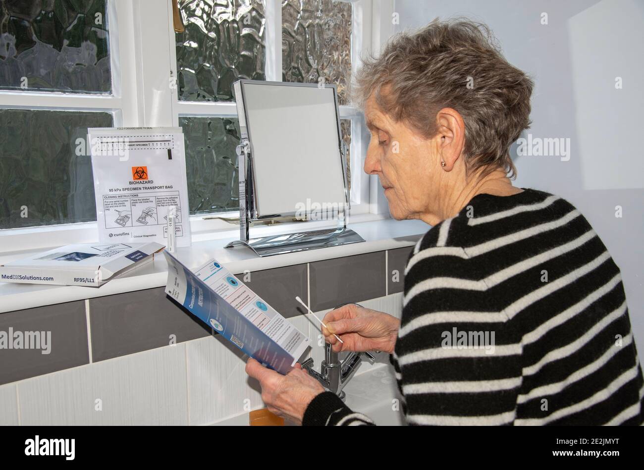 Inghilterra, Regno Unito. 2021. Donna in bagno che studia le istruzioni di un Coronavirus, Covid-19 Home Test kit Foto Stock