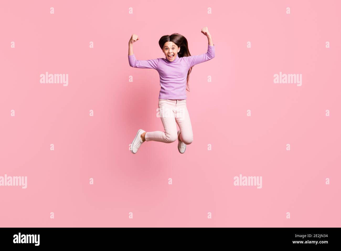 Foto a lunghezza intera di spettacolo di salto di bambina pazza piccola le mani tricipite indossano pantaloni viola in pullover isolati di colore rosa sfondo Foto Stock