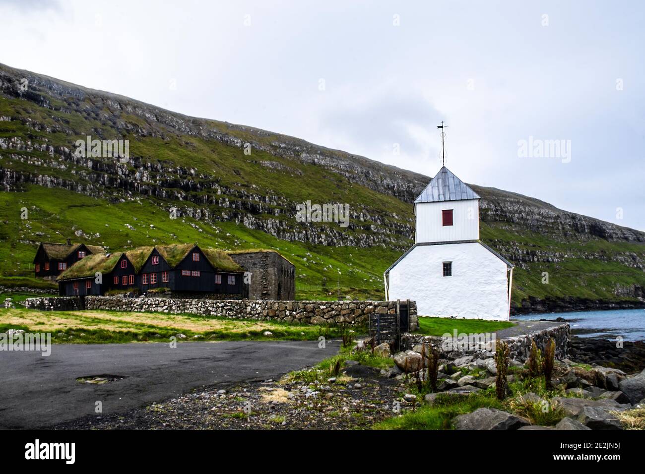 Villaggio di Kirkjubøur su Streymoy, Isole Faroe: Spettacolare Chiesa di San Olav e vecchia casa colonica dipinto di nero e tetto di erba. Foto Stock