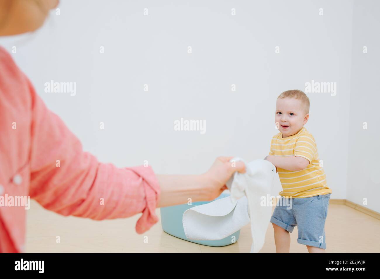 Il figlio giovane aiuta la mamma a mettere il bucato pulito dopo il lavaggio dentro cestino Foto Stock