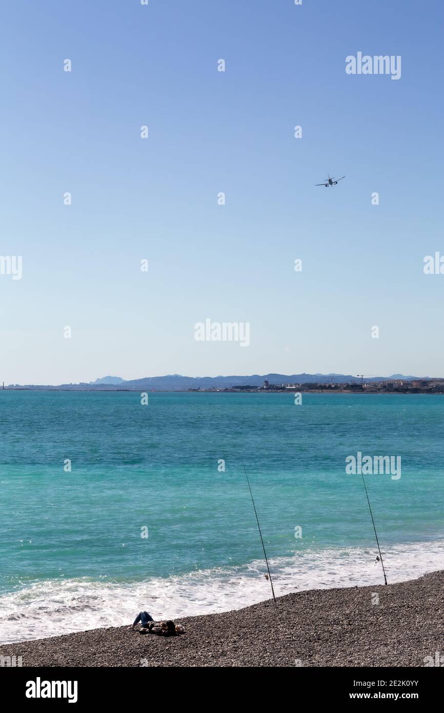 Vista sull'oceano mentre i pescatori si rilassano sulla spiaggia mentre un aereo vola in aeroporto Foto Stock