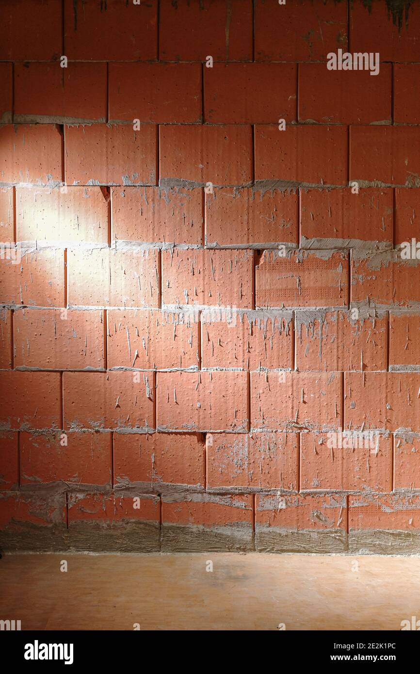 Parete ruvida di mattoni da blocchi di argilla di stile Porotherm in un sito di costruzione illuminato lateralmente, sfondo di architettura con spazio di copia, verticale Foto Stock