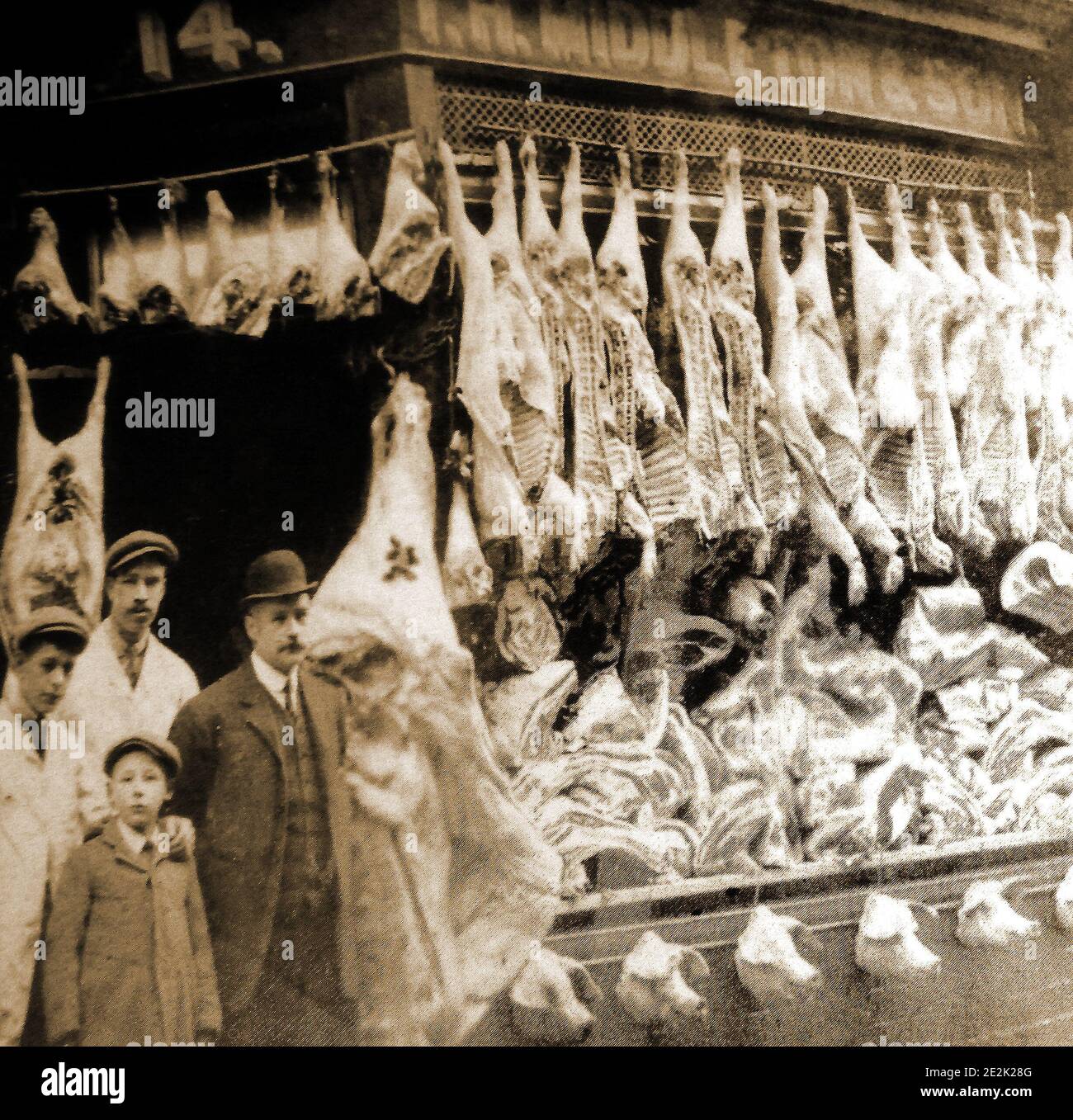 Una prima fotografia di un macellaio tradizionale a Whitby, nel Nord Yorkshire, Inghilterra. Il proprietario del negozio, la sua famiglia e il personale posa alla porta, whils la finestra contiene una massiccia esposizione di carne (compresa una fila di teste di maiale) probabilmente al tempo di Natale. Foto Stock