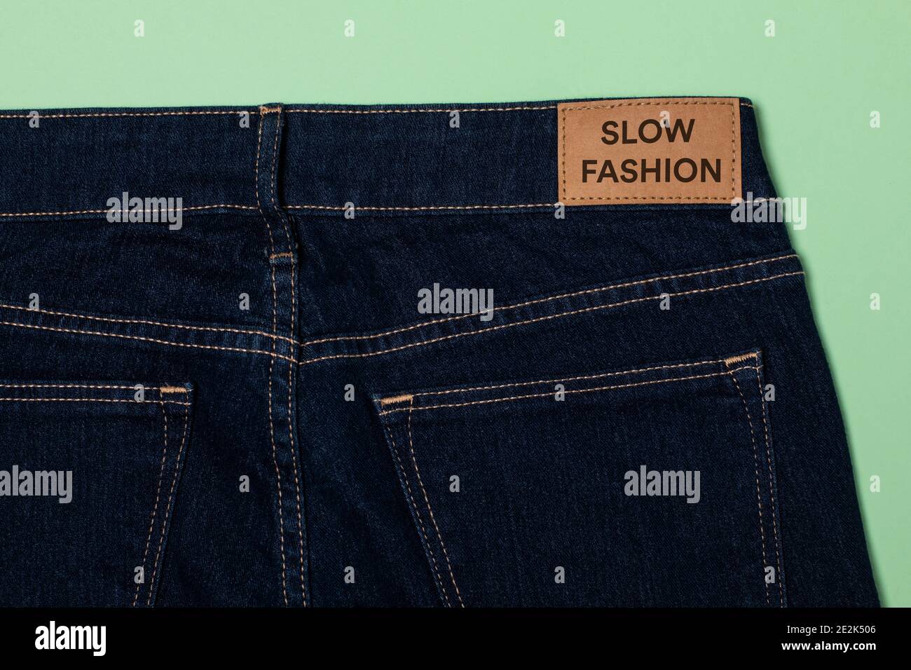Jeans denim con un'etichetta di abbigliamento che dice moda lenta. Concetto di zero sprechi. Riutilizzando abiti e tessuti riducendo gli sprechi di moda. Orizzontale piatto Foto Stock