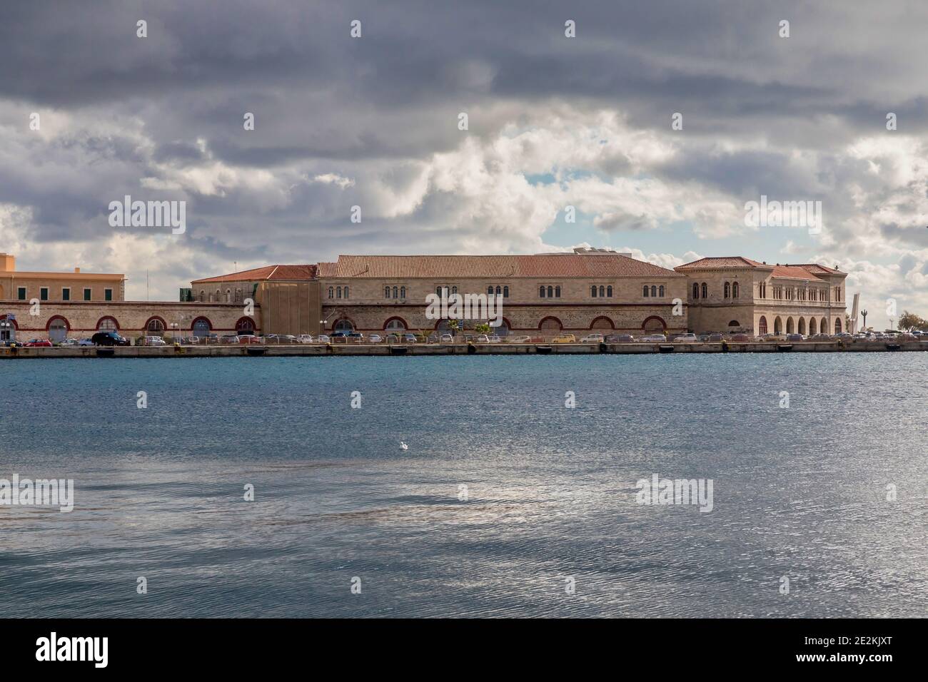 Porto di Ermoupolis con edifici cittadini sullo sfondo. Un solo gabbiano che nuota in mare. Immagine stock. Foto Stock