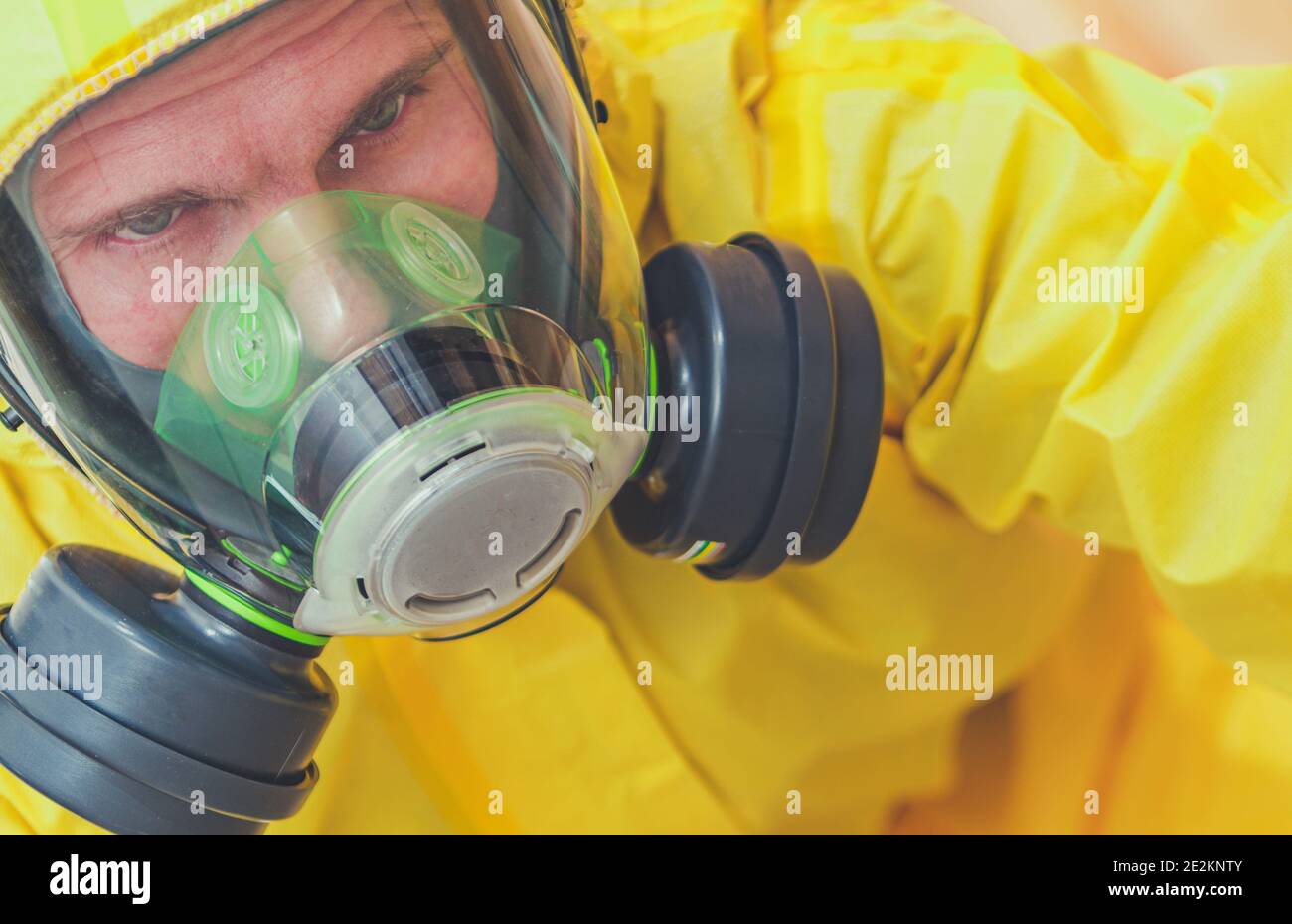 Stanco lavoratore caucasico nei suoi anni '40 indossando tuta gialla Hazmat e maschera facciale totale di protezione del respiro. Zona di rischio biologico. Tema industriale. Foto Stock