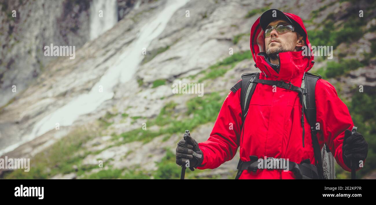 Sport all'aperto e tema ricreativo. Hiker caucasico negli anni '30 indossando Raincoat rosso e occhiali Safety Sport sulla Scenic Alpine Trailhead. Rocce e. Foto Stock