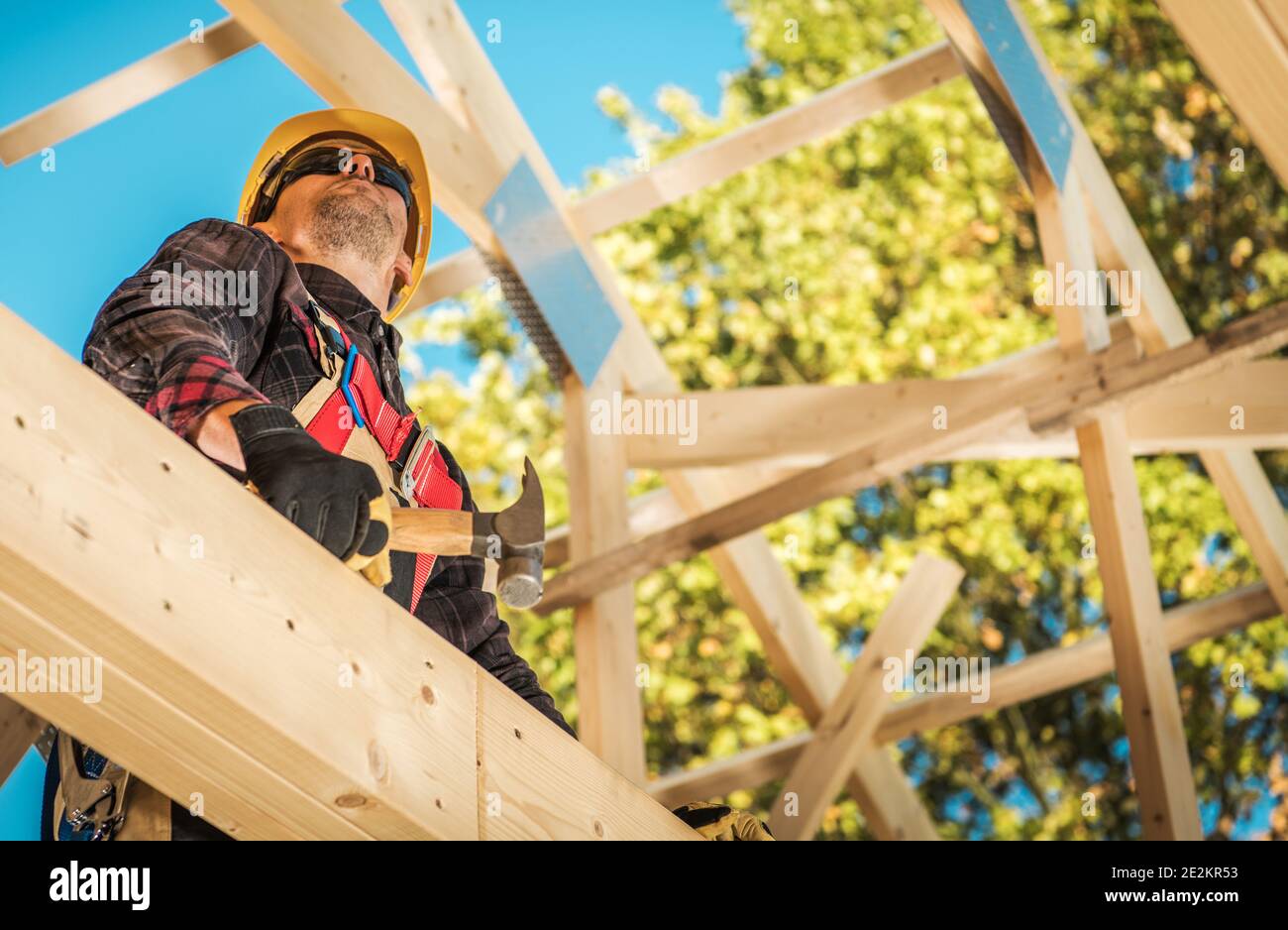 Caucasico lavoratore di costruzione nei suoi 40s tra gli elementi del tetto di legno del telaio della Casa Skeleton. Tema dell'industria delle costruzioni. Foto Stock