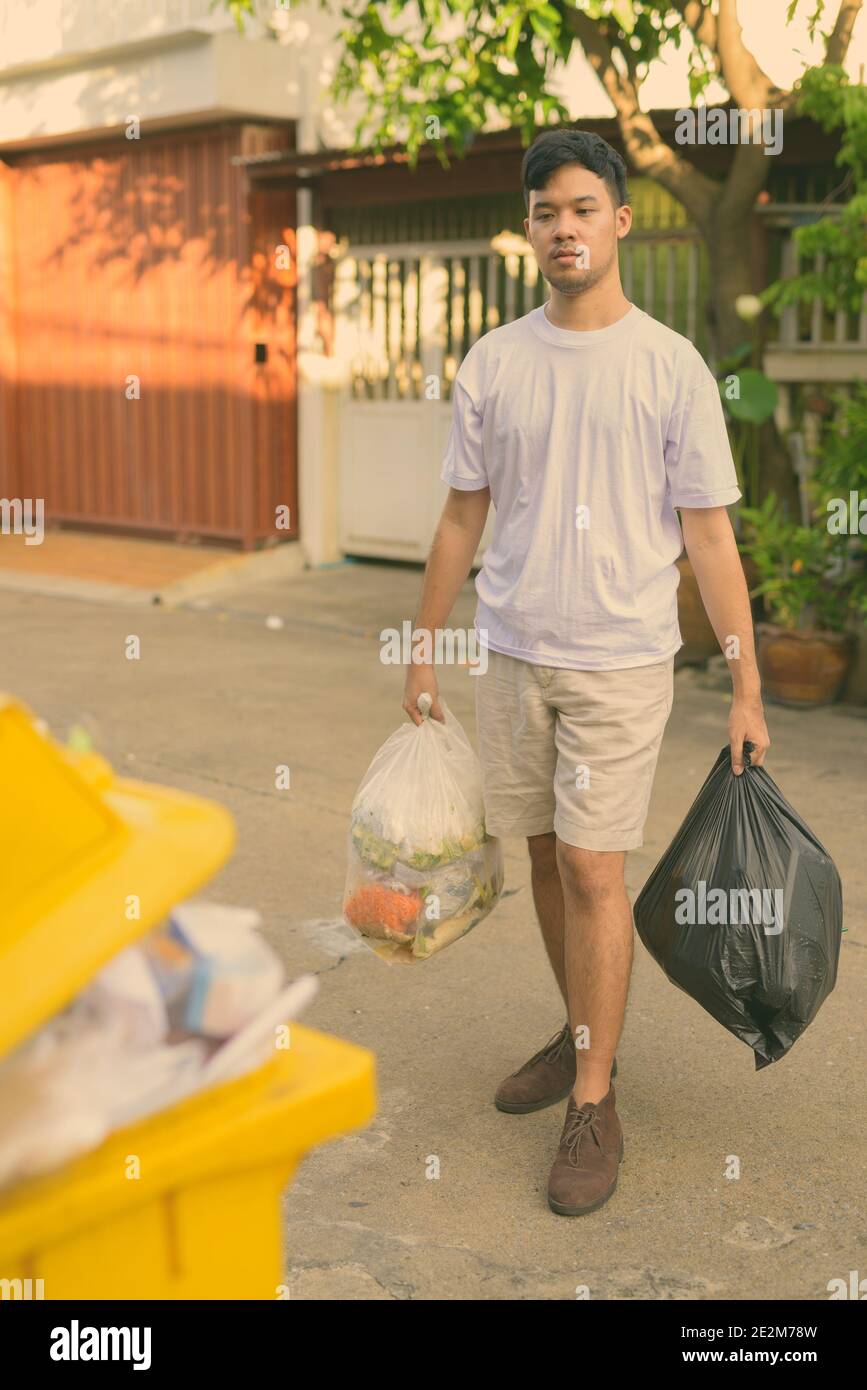 Giovane uomo asiatico tenendo fuori la spazzatura a casa Foto Stock