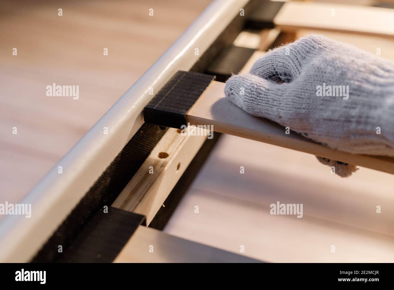 Mano del lavoratore maschile nel letto di assemblaggio dei guanti, che collega le doghe al telaio del letto Foto Stock