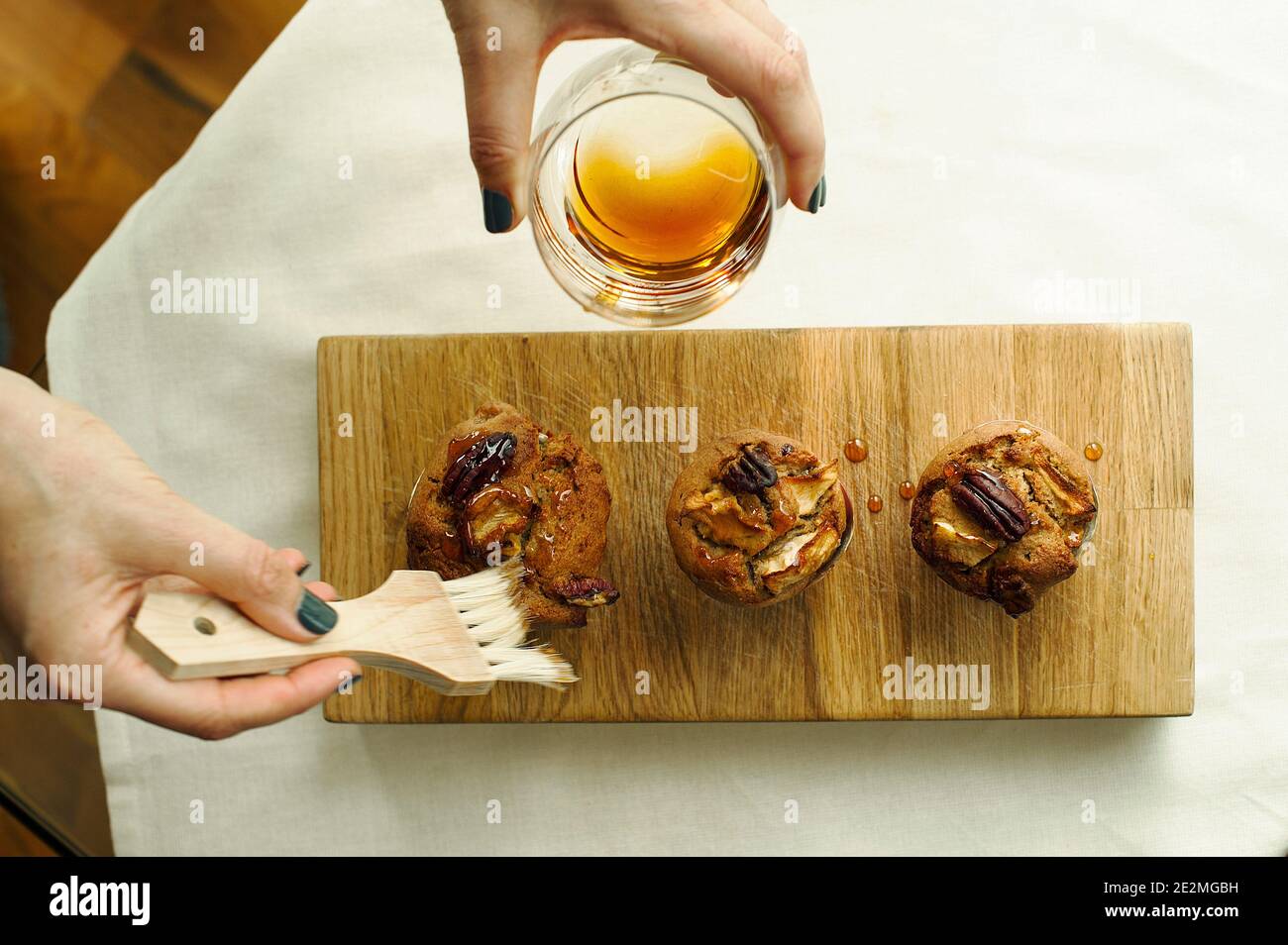 Vista dall'alto delle mani della donna che inumidisce i muffin di mela pecan alla cannella con sciroppo dolce. Panificazione fatta in casa, gourmet, senza glutine Foto Stock