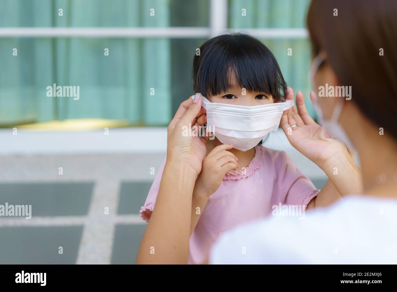 Madre asiatica aiutare sua figlia indossare maschera di protezione per proteggere il coronavirus Covid-19 focolaio situazione prima di andare a scuola. Preparati a scuola Foto Stock