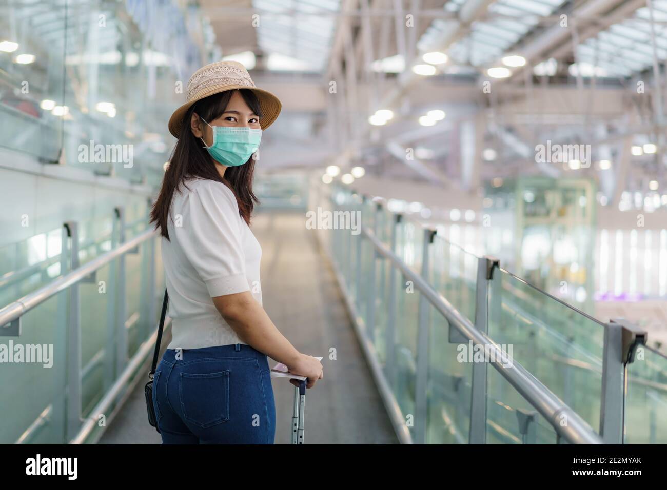 Donna asiatica viaggiatore che indossa maschera a piedi per salire a bordo del terminal dell'aeroporto e guardare la macchina fotografica e sorriso. Donna passeggero che viaggia in p Foto Stock