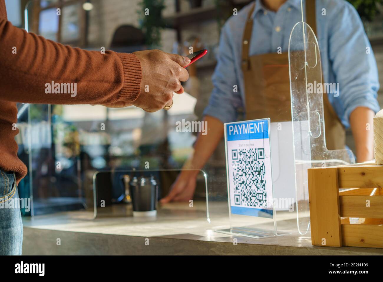 Cliente asiatico che utilizza il pagamento tramite scansione mobile QR o NFC su smartphone pagare per la sua bevanda di caffè in caffè Negozio e plexi schermo e Barista indossare Foto Stock