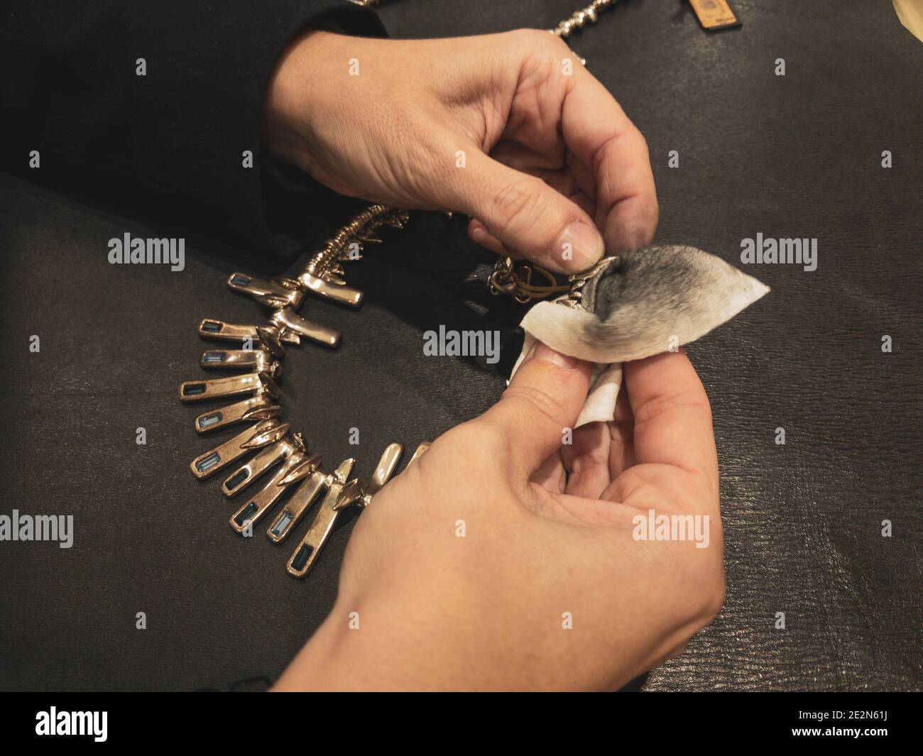Donna mani che puliscono la collana argento designer con panno, strofinando brillare Foto Stock
