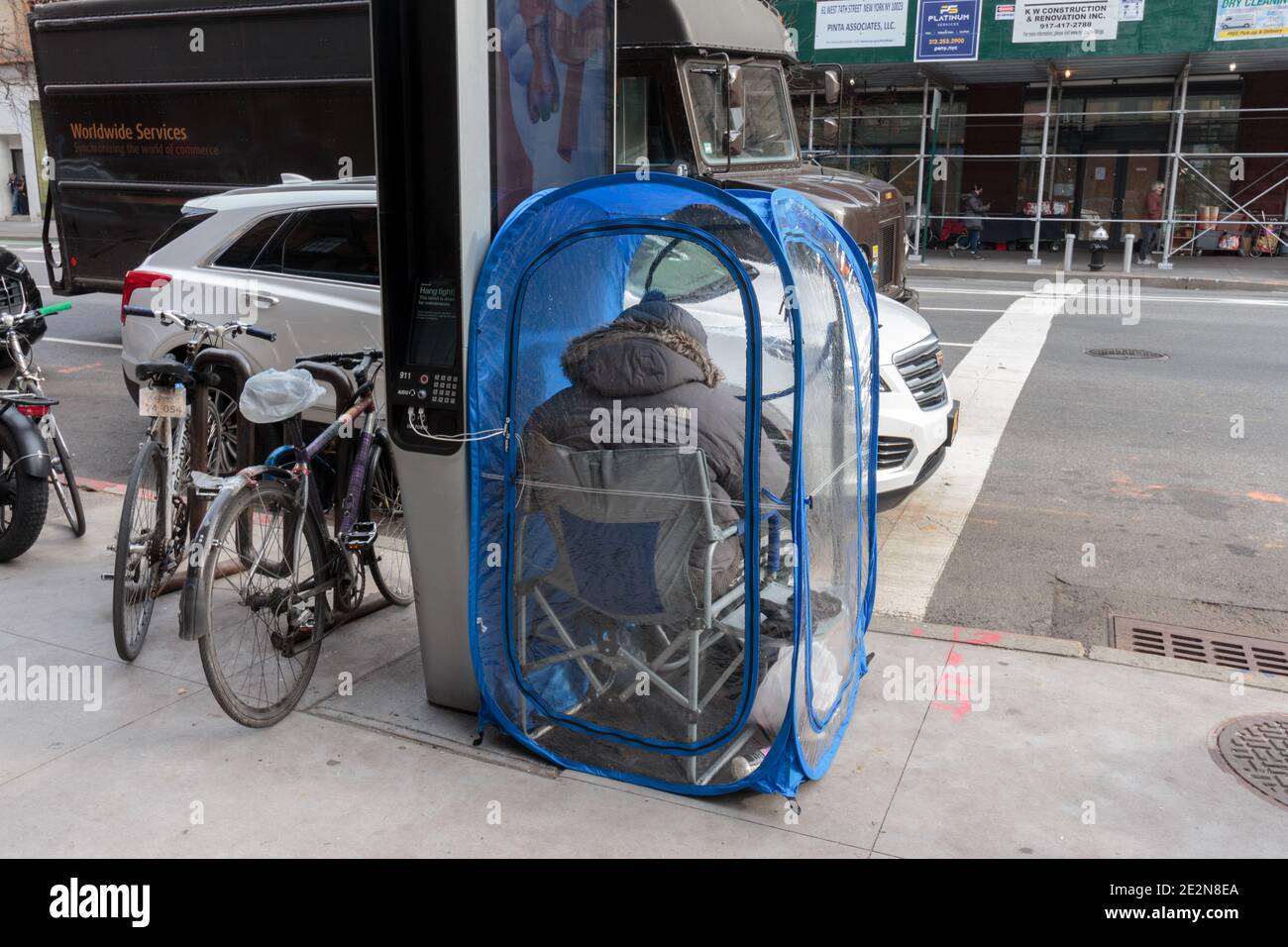 una persona si siede in un cestino pop-up di plastica personale sopra Un angolo di New york City Street in inverno vicino una stazione di ricarica elettrica pubblica Foto Stock
