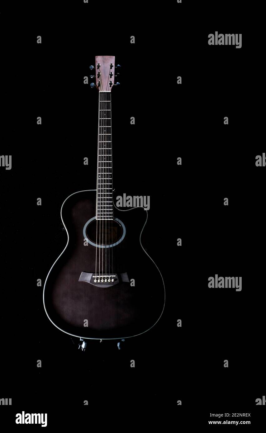 chitarra acustica nera con un profilo bianco intorno ad esso su sfondo nero, posto su un supporto in posizione verticale, tasto spazio copia basso Foto Stock