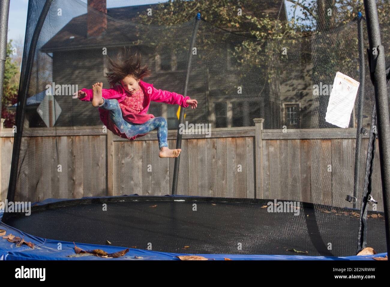 Una bambina gioiosa con i capelli selvaggi salta sul trampolino con rete a rete Foto Stock