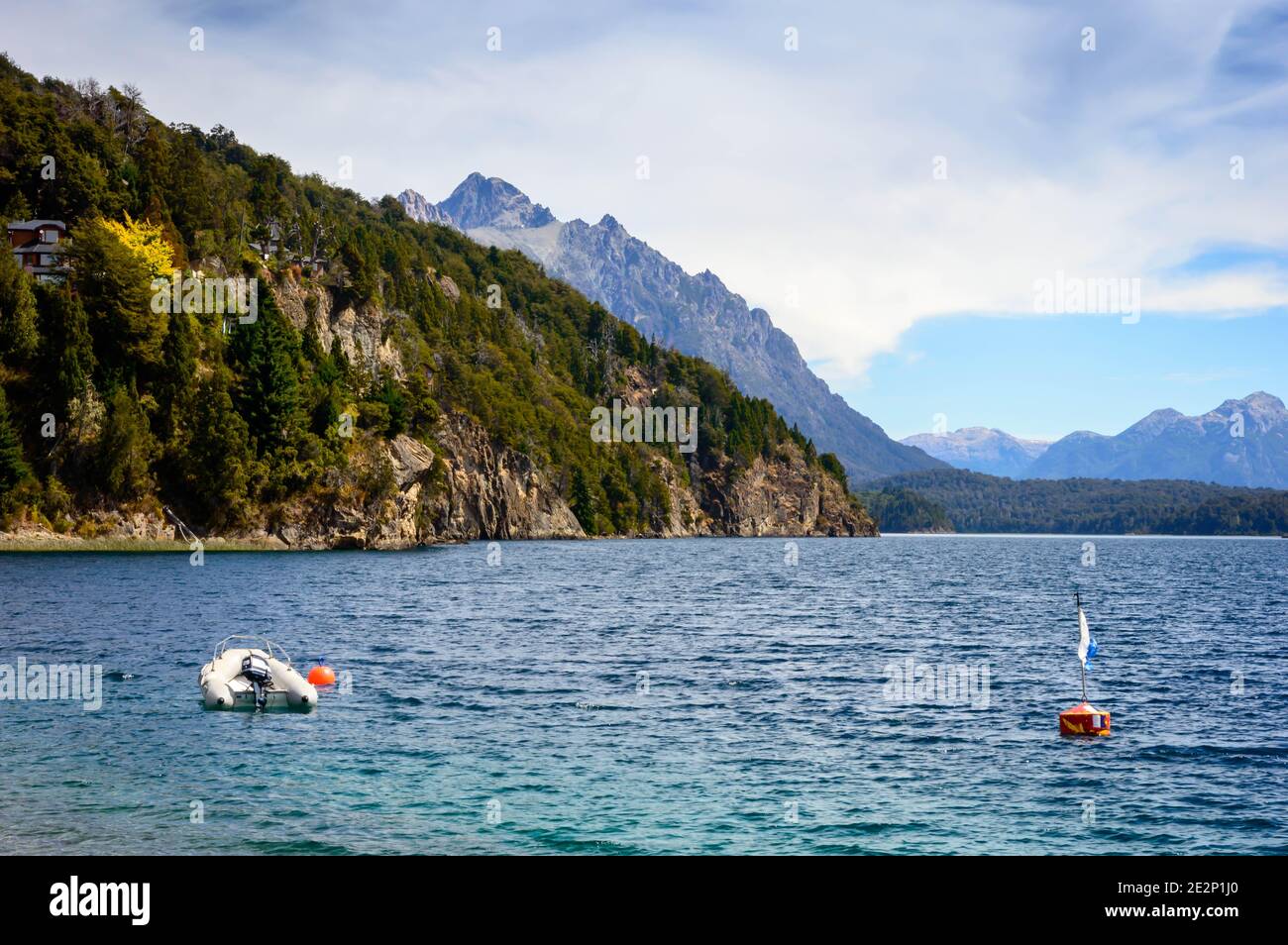 Riva del lago con rocce, montagne e pini. Un motoscafo che galleggia vicino a una boa. Estate a Bariloche. Foto Stock