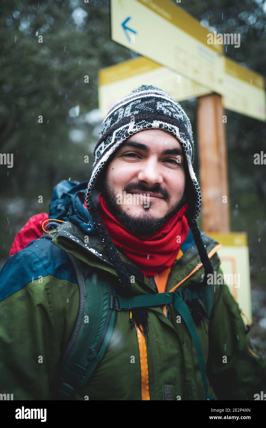 Uomo sorridente alla macchina fotografica con protezione dal freddo accanto a a. cartello trekking Foto Stock