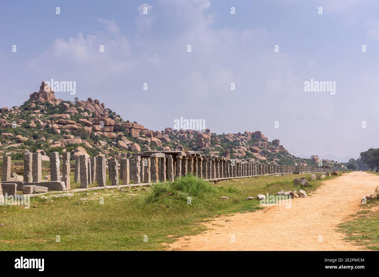 Hampi, Karnataka, India - 5 novembre 2013: Sentiero giallo che conduce al Tempio di Vijaya Vitthala. Fila di colonne di pietra grigia con colline verdi piene di br Foto Stock