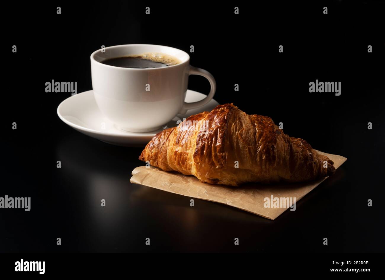 Un croissant e un caffè caldo su sfondo nero Foto Stock