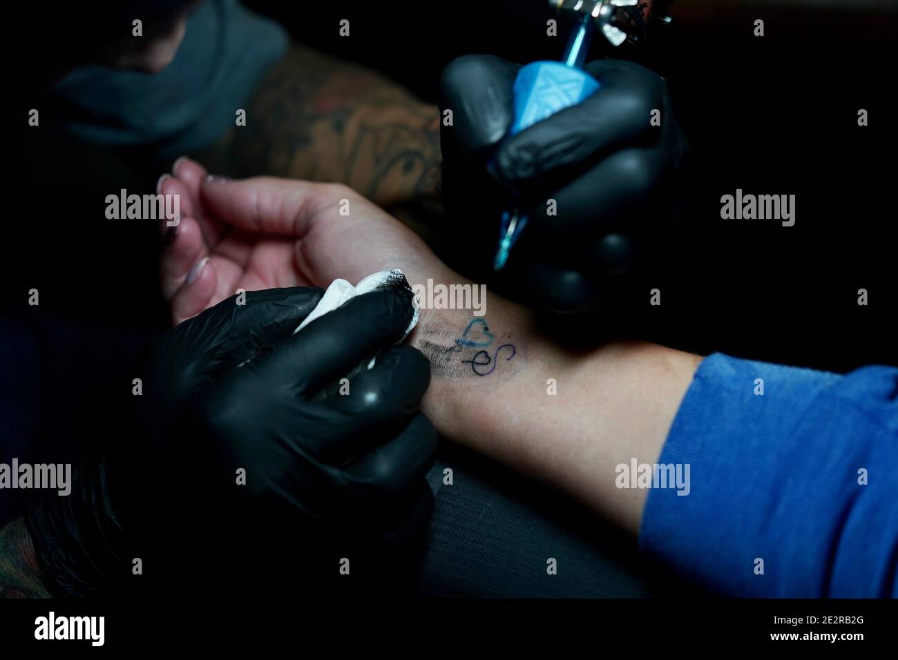 Una vista ravvicinata di una donna che riceve la lettera "s" con un cuore tatuato all'interno del polso. Foto Stock
