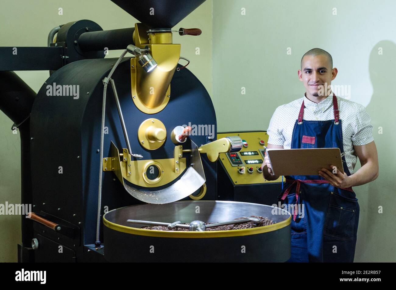 Le mani dell'uomo arrostire i chicchi di caffè aromatico su un moderno macchina utilizzata per tostare i fagioli Foto Stock