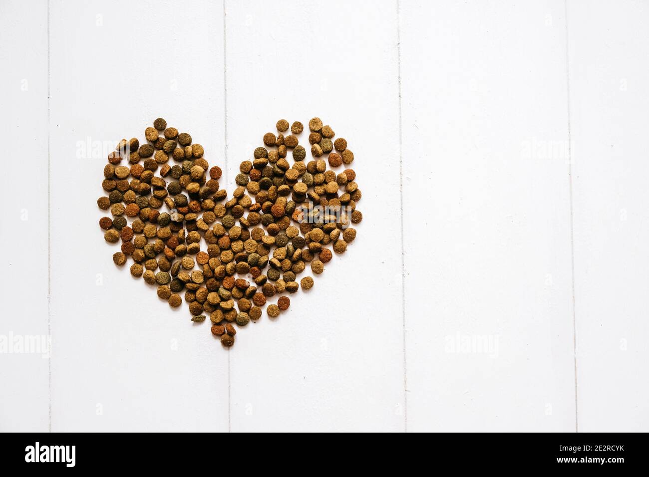 Cibo di gatto essiccato con una forma di cuore su sfondo bianco. Vista dall'alto cibo marrone per animali domestici su sfondo bianco di legno con spazio di copia del testo. Foto Stock