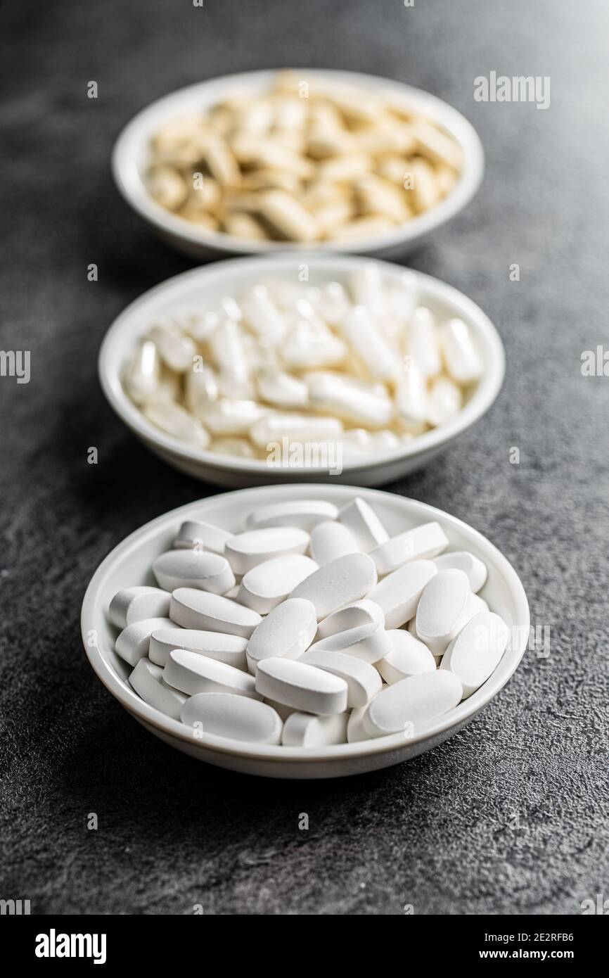 Pillole mediche bianche. Pillole, compresse e capsule di medicina farmaceutica in ciotola su tavola nera. Foto Stock