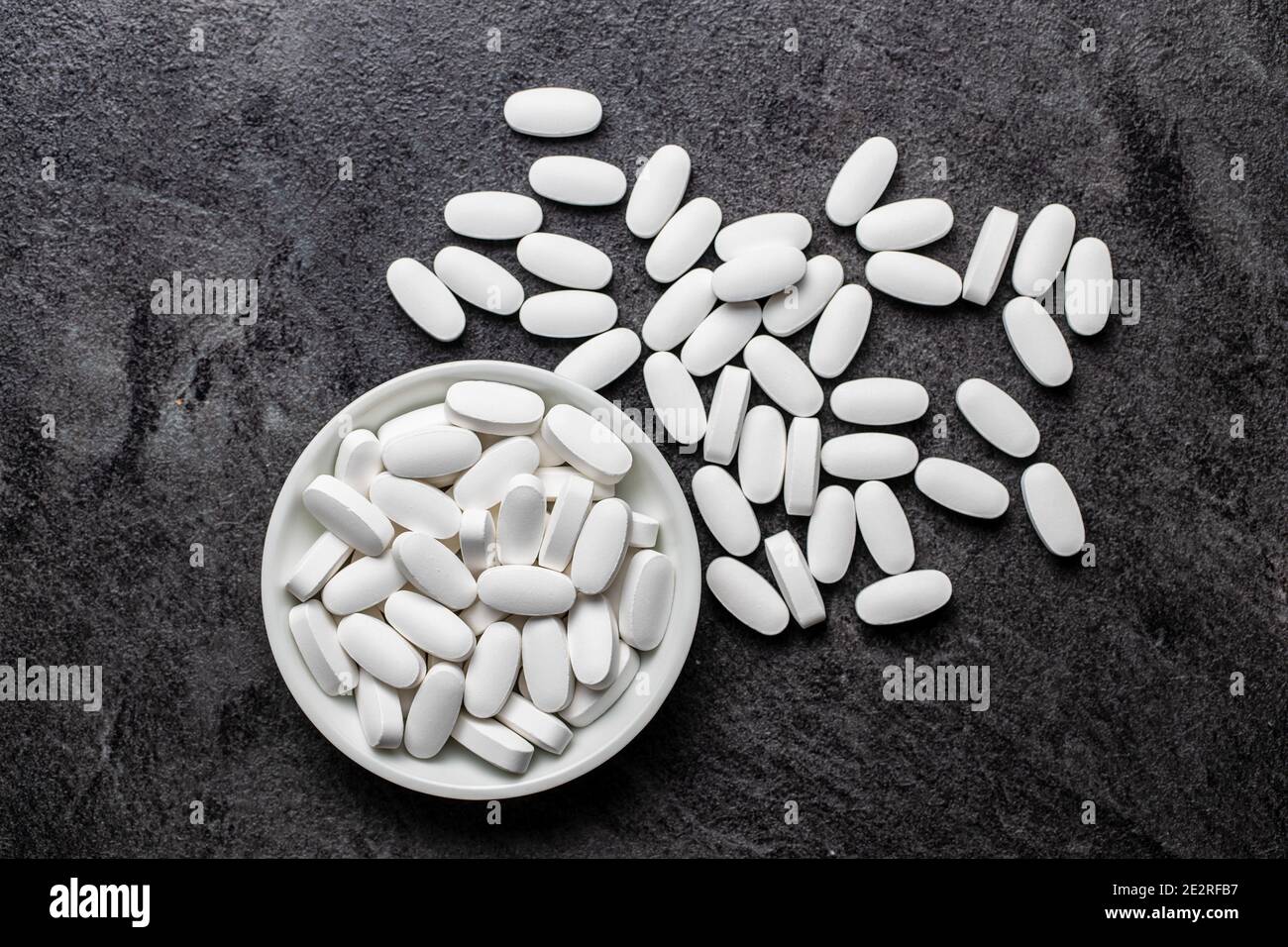 Pillole mediche bianche. Pillole, compresse e capsule di medicina farmaceutica in ciotola su tavola nera. Vista dall'alto. Foto Stock