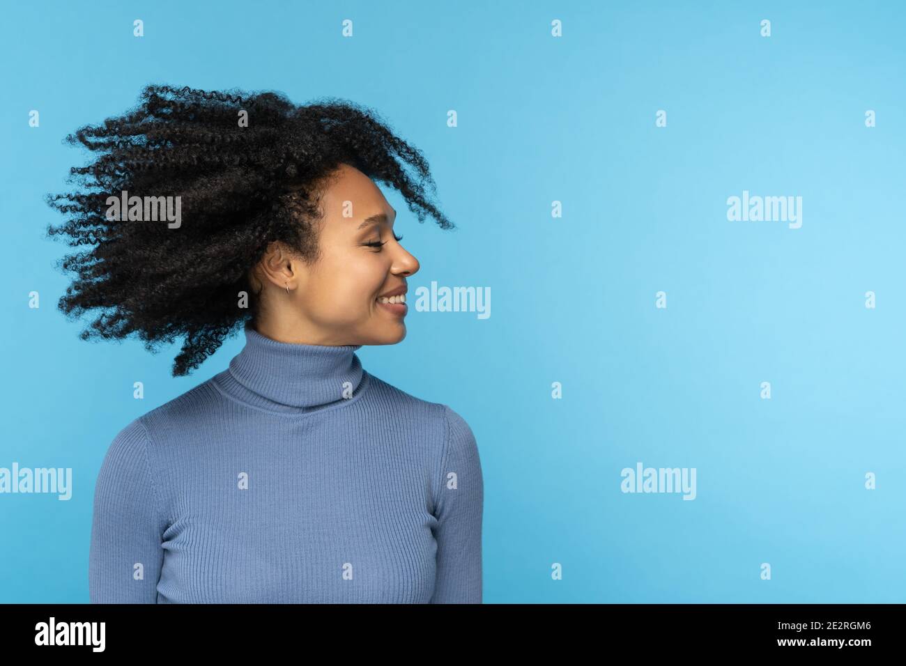 Felice Afro donna sorridente, ha buon umore, ballando con i suoi capelli neri ricci volare, isolato su blu Foto Stock