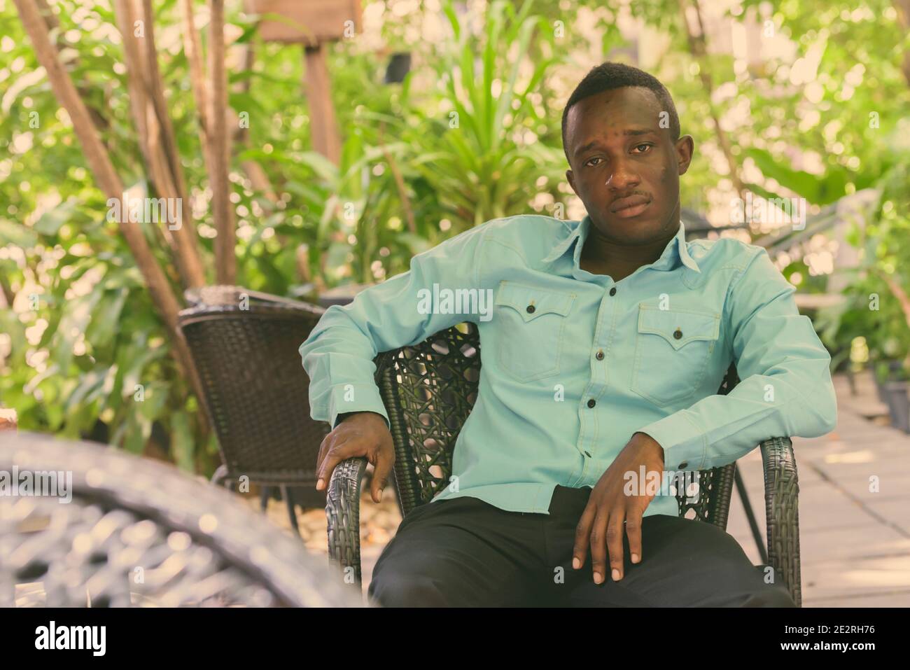 Giovane Africano nero uomo seduto al outdoor coffee shop circondati dalla natura Foto Stock