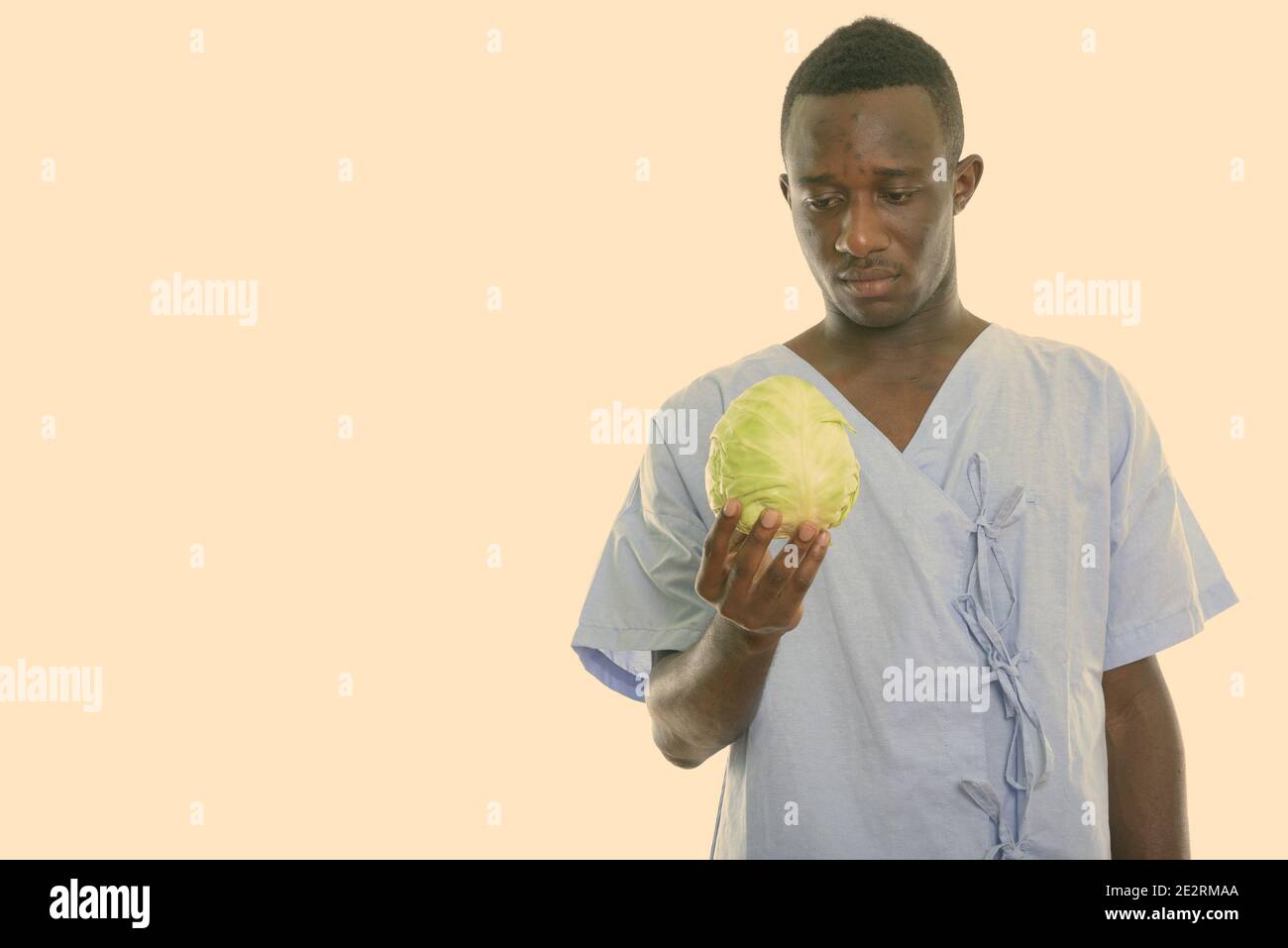Studio shot del giovane africano nero uomo paziente holding e guardando il cavolo verde Foto Stock