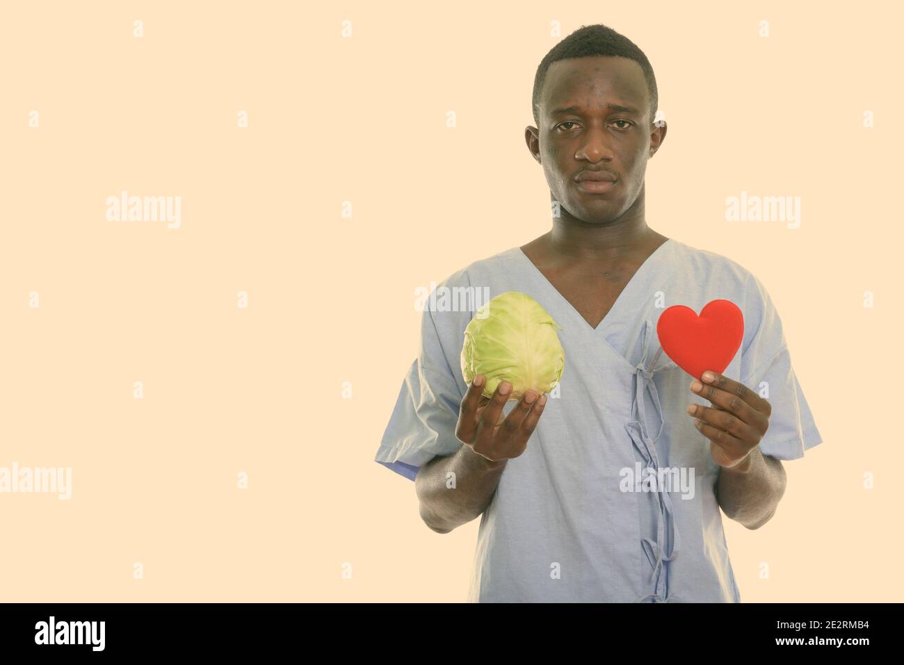 Studio shot del giovane africano nero uomo paziente tenendo cavolo verde e cuore rosso Foto Stock