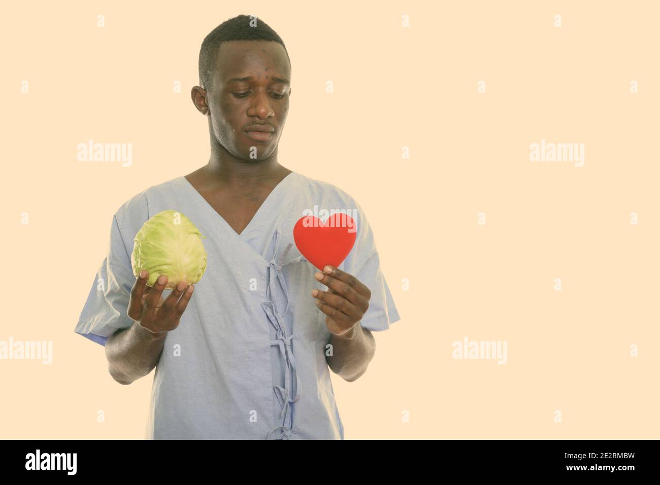 Studio shot del giovane africano nero uomo paziente tenendo cavolo verde e guardando il cuore rosso Foto Stock