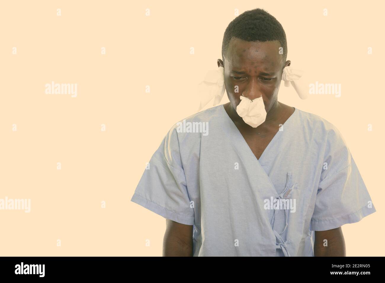 Studio shot di giovani neri africani paziente uomo guardando verso il basso e malati con i tessuti nel suo il naso e le orecchie Foto Stock