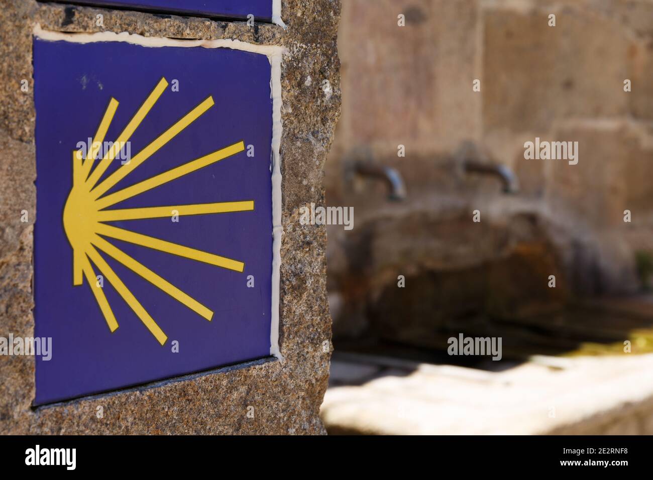 St.James Way, segno giallo del cuoio capelluto con una fontana sullo sfondo, Finisterre, Galizia, Spagna Foto Stock