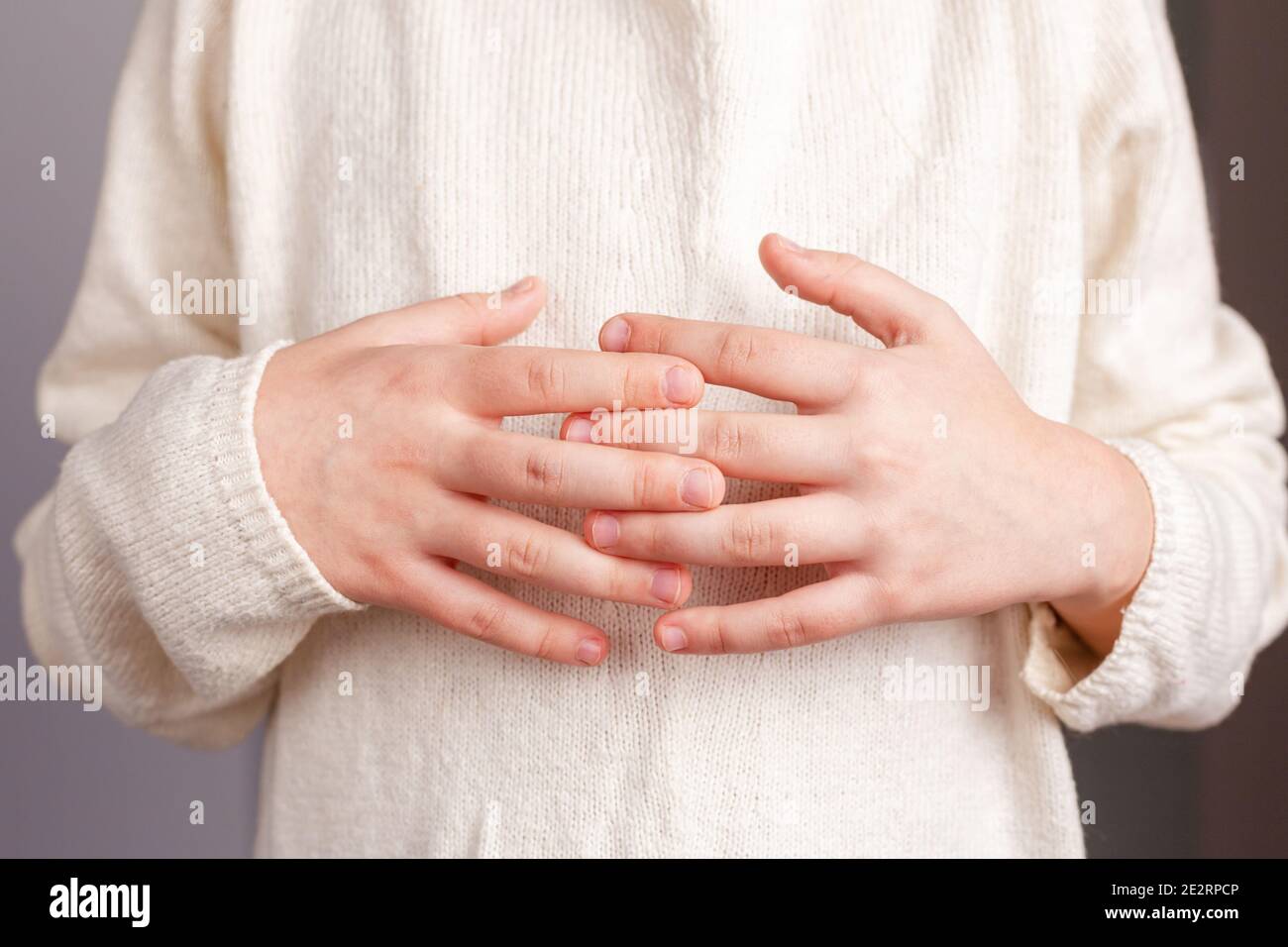 Primo piano delle mani di un bambino ripiegate sullo stomaco con le dita intrecciate, in un maglione leggero lavorato a maglia color champagne Foto Stock