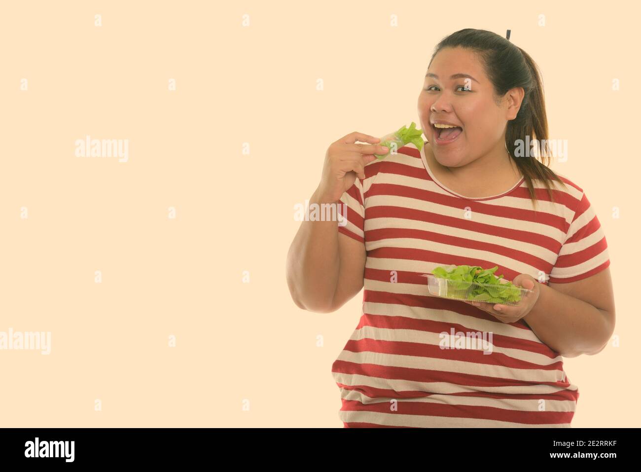 Studio shot di giovani felici fat donna asiatica sorridere mentre di mangiare verdura fresca wrap Foto Stock