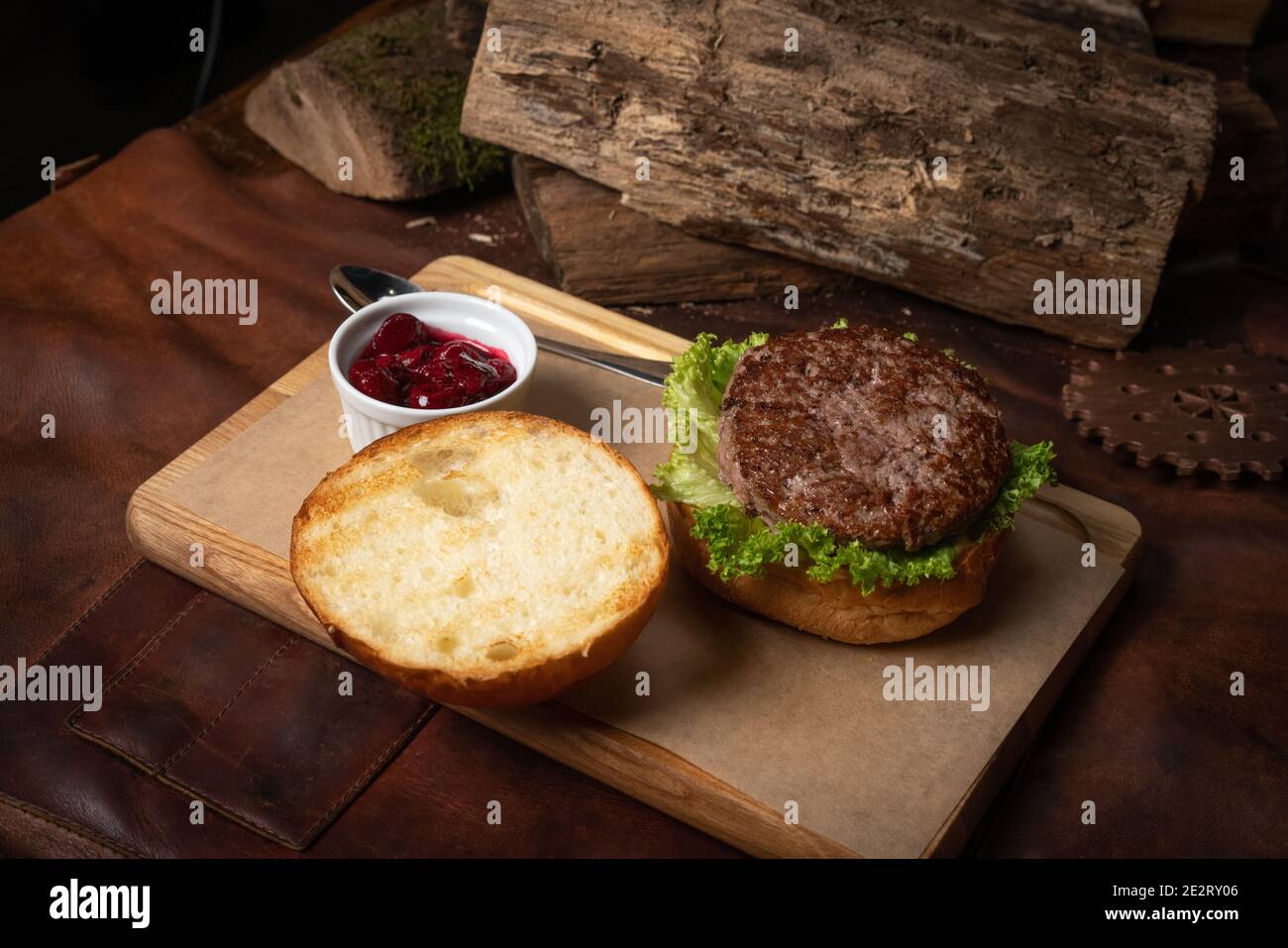 Hamburger di manzo fresco artigianale con salsa di ciliegia in un recipiente per salsa, lattuga fresca con panna di piombo che si posa accanto con logge di legno come decorazione. Ristorante Foto Stock