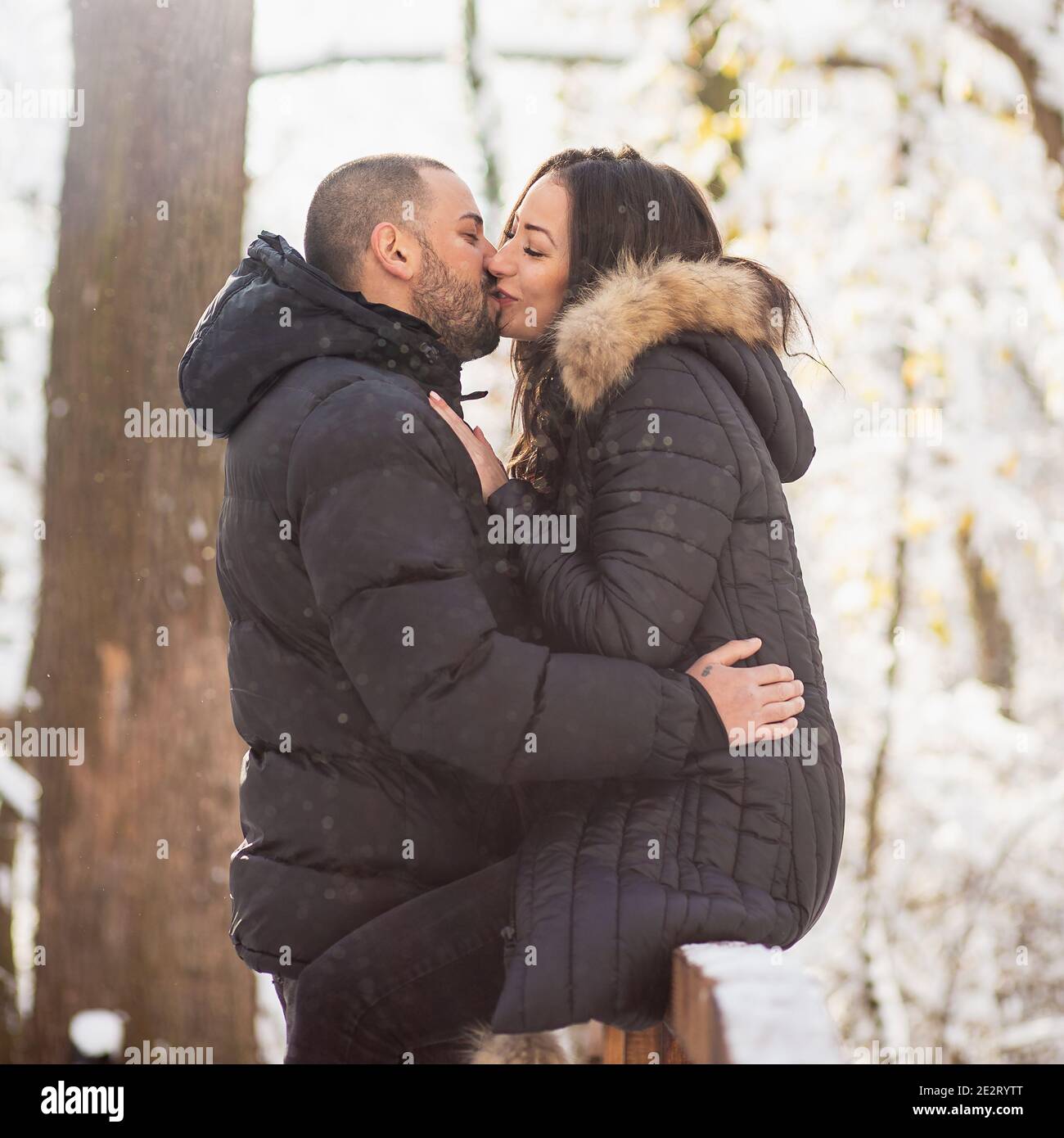 Uomo e donna innamorati abbracciando e baciando su un ponte. Neve sfondo invernale. Foto Stock