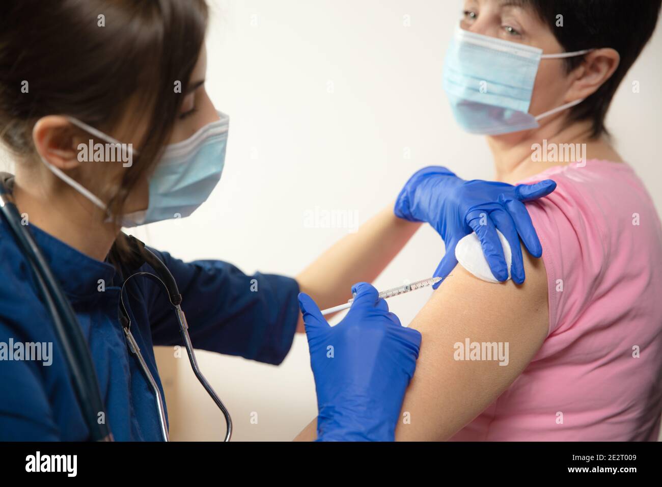 Salute. Primo piano medico o infermiere che somministrano il vaccino al paziente utilizzando la siringa iniettata. Funziona in maschera facciale. Protezione contro il coronavirus, la pandemia COVID-19 e la polmonite. Sanità, medicina. Foto Stock